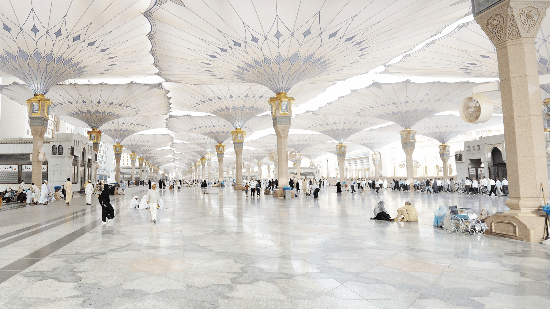 Expansive home within the prophet's mosque in Medina with pilgrims and retractable umbrellas.